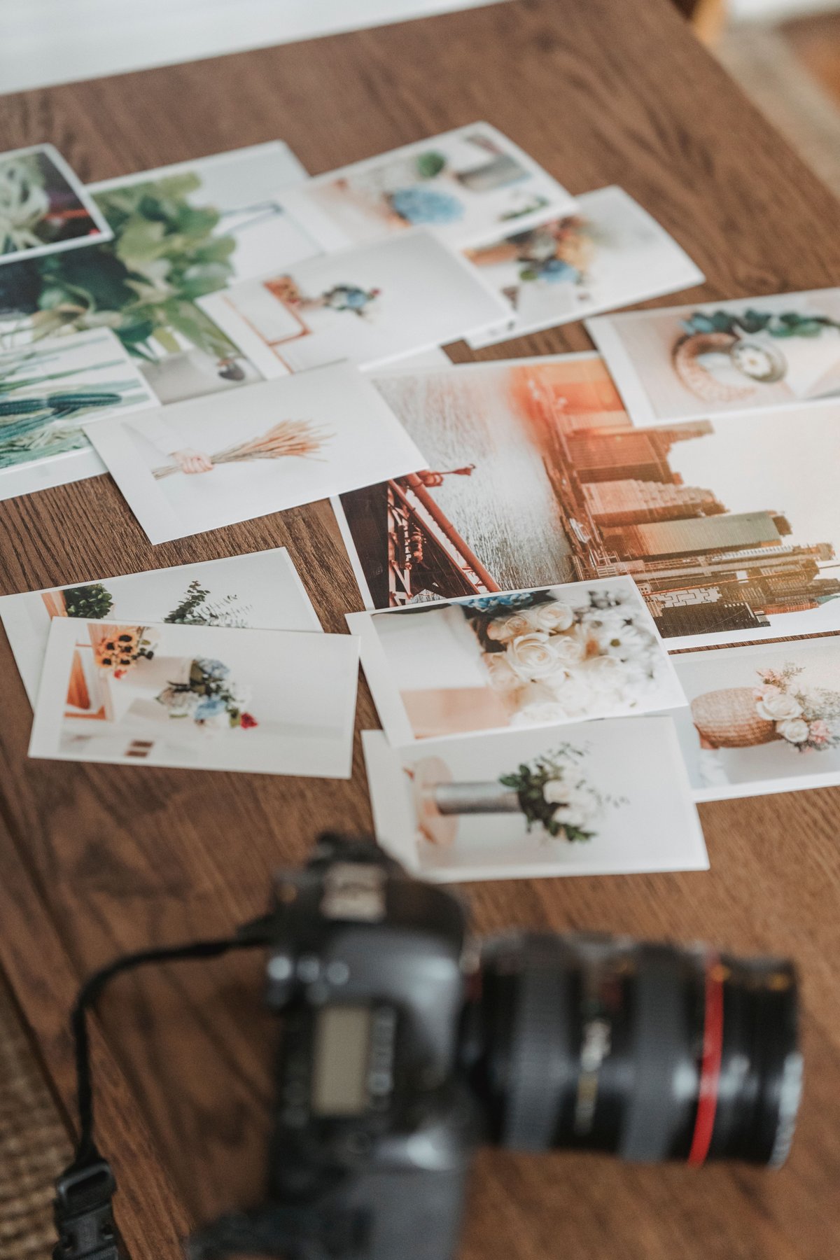 Several photographic prints arranged on a wooden table beside a camera.